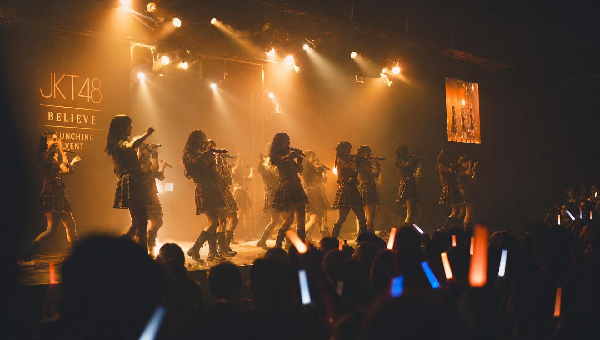 Panggung teater JKT48 dengan cahaya tungsten dan penonton bersama glow stick